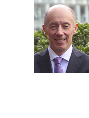 Peter Diamond wears a dark suit and purple tie, smiling against a leafy green background.